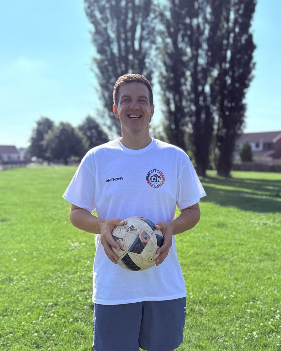 Anthony, Costa Ballers head coach, smiling on the pitch with a football