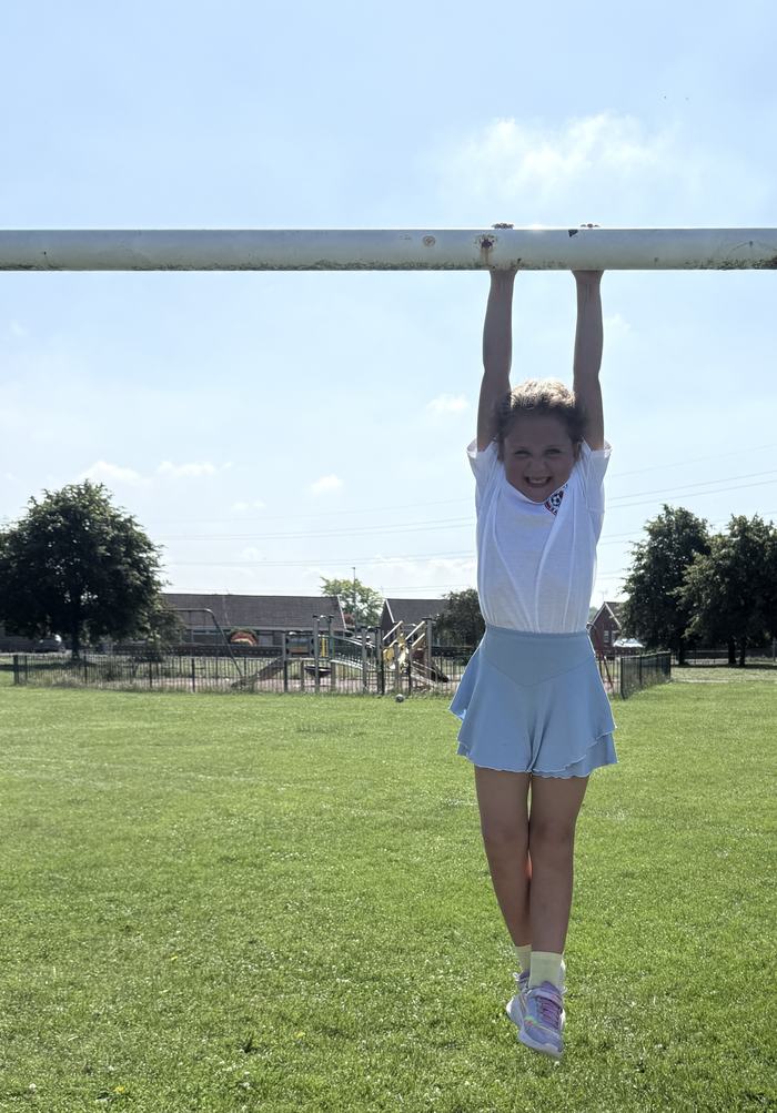 Girl hanging happily from the goalpost, all smiles